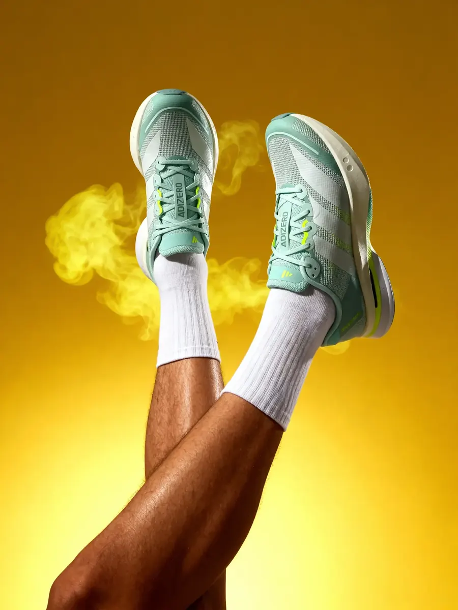 Mint running shoes raised against a yellow smoke cloud